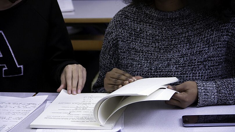 Zwei junge Menschen sitzen vor einem Buch und lernen gemeinsam
