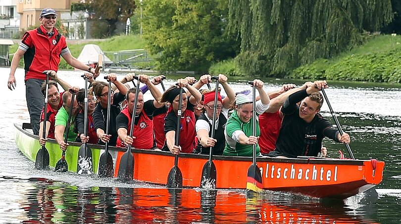 Ein Team von ca 15 Personen sitzt in einem Drachenboot beim Rudern.