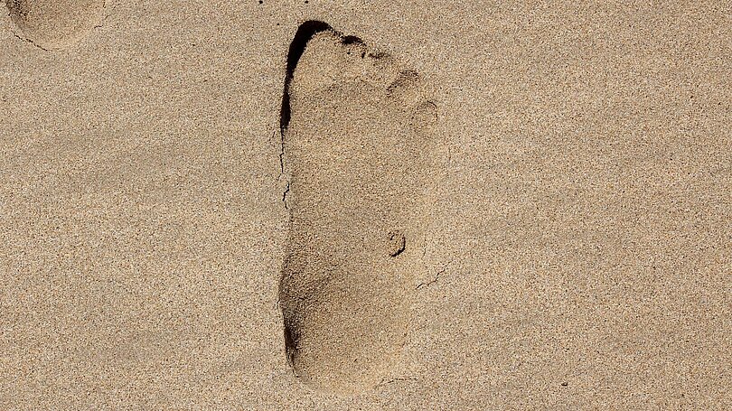 Eine einzelne Fußspur im nassen Sand.