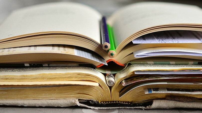 Ein Stapel aufgeschlagener Bücher mit eingelegten Stiften und Zetteln.