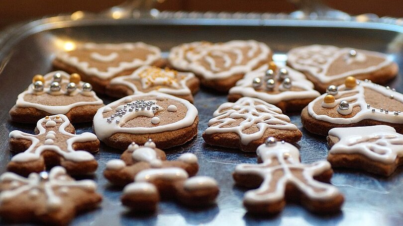 Verziehrte Lebkuchen in Form von Herzen, Bäumen und Männchen liegen auf einem silbernen Tablett. 