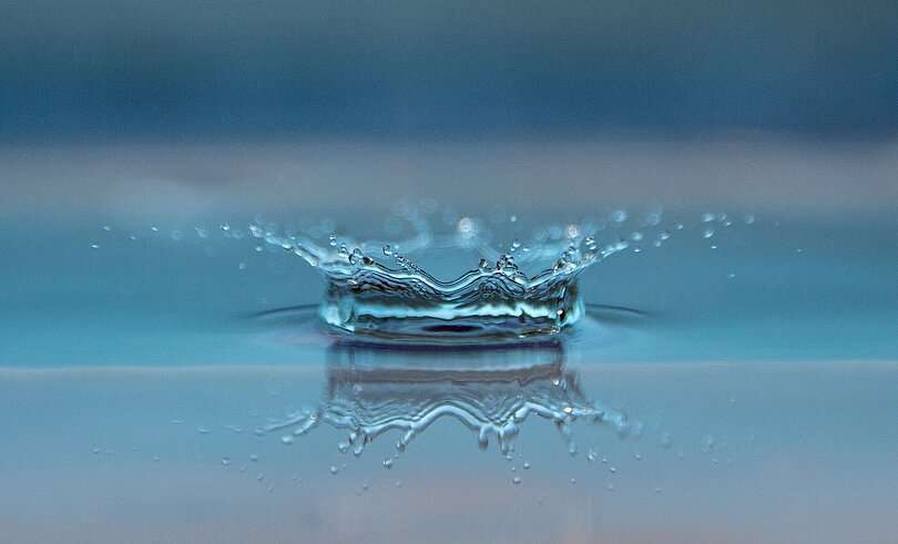 Ein Wassertropfen fällt auf eine glatte Wasseroberfläche.